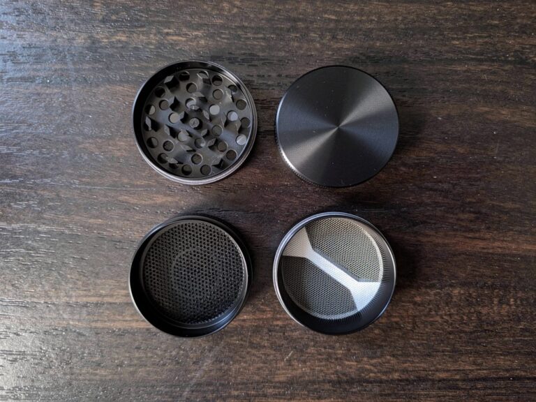 Disassembled 4-piece herb grinder parts laid flat on dark wood