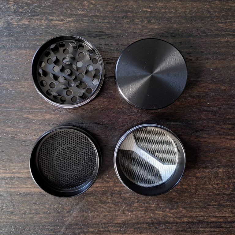 Disassembled 4-piece herb grinder parts laid flat on dark wood