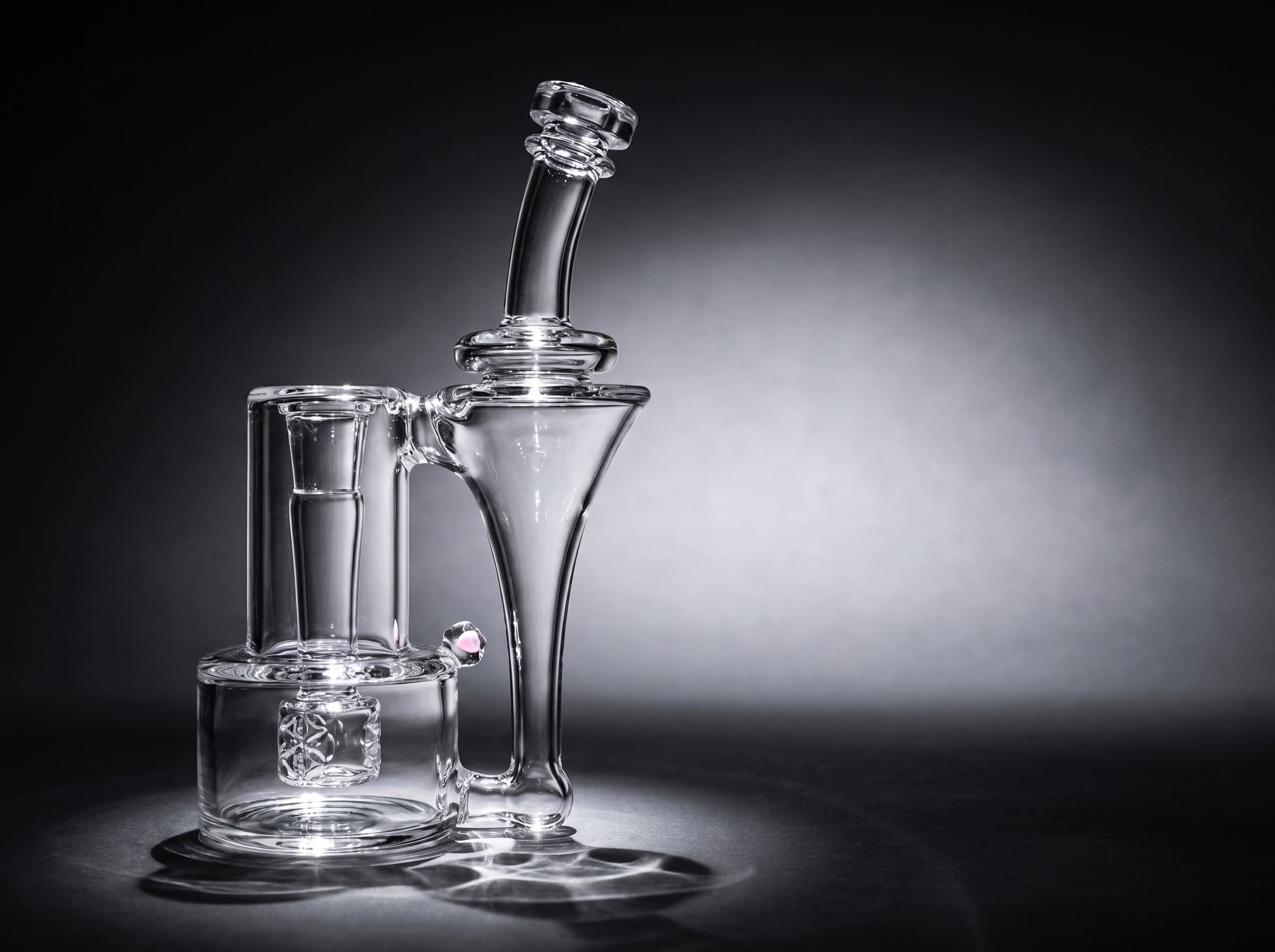A clear glass recycler dab rig lit by a single spotlight